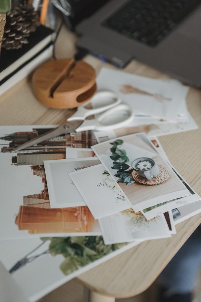 From above of various images scattered on wooden table near netbook for remote work from home