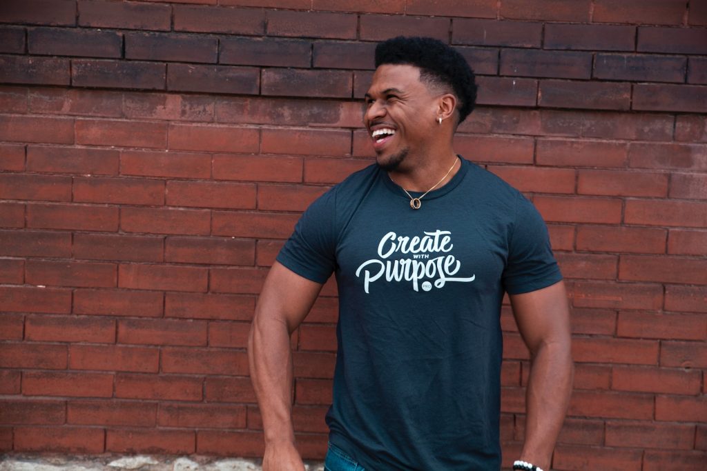 man in blue crew neck t-shirt standing near brown brick wall